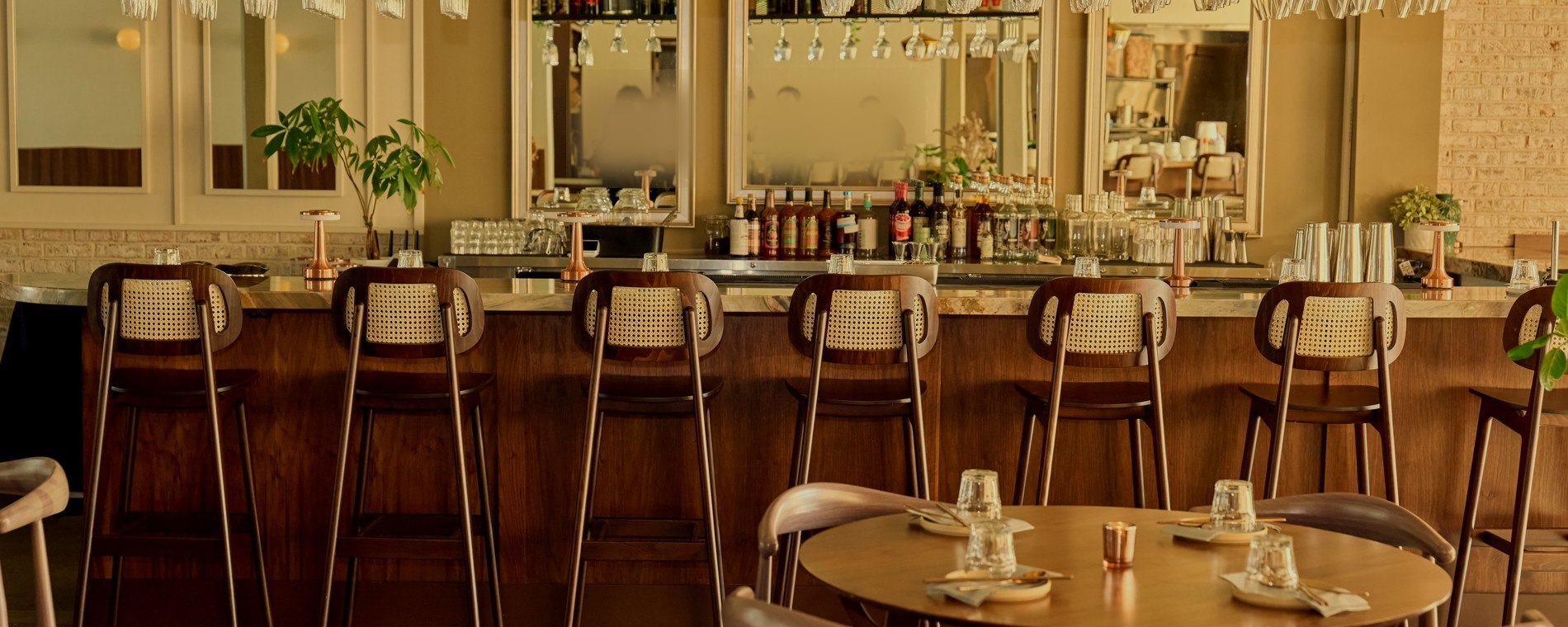 The walnut bar at Danbi in the evening, cane-back stools, copper accents and glassware under warm light